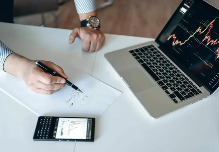 Analiza wykresów na laptopie i telefonie, notatki na papierze. To może być przygotowanie do gry na giełdzie, jak na stooq.