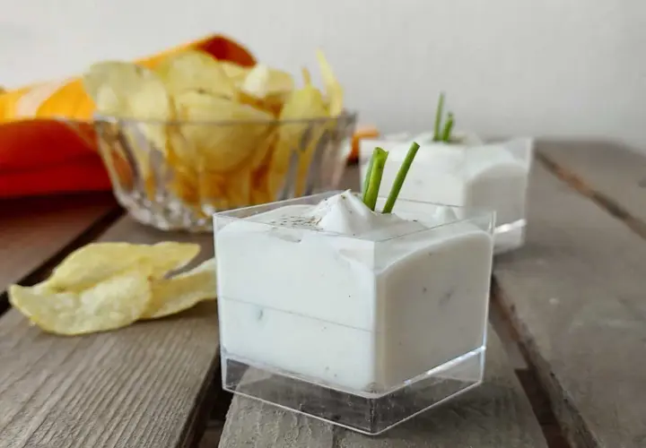 Salsa yogurt cremosa, guarnita con erba cipollina, pronta per accompagnare patatine croccanti.