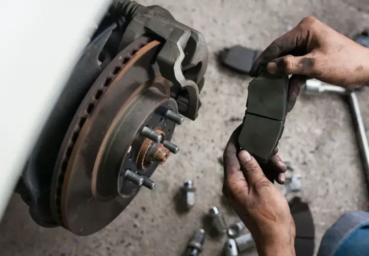 Mechanik pokazuje zużyte klocki hamulcowe przed wymianą.
