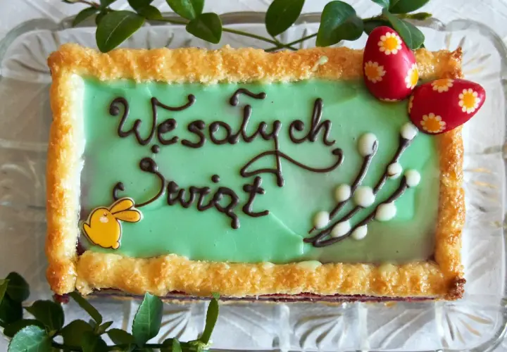Zielone ciasto wielkanocne z napisem "Wesołych Świąt", ozdobione zajączkiem, baziami i pisankami.