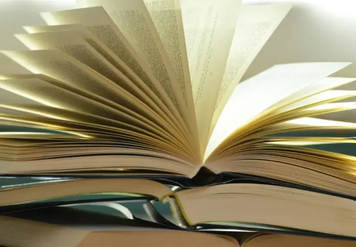 Otwarta książka na stosie innych. Różnica między romansem a literaturą obyczajową z wątkiem miłosnym jest jak między stronami tej książki – subtelna, lecz znacząca.