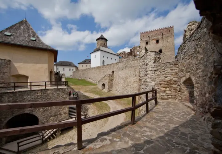 Kamienne mury i wieże zamku Stará Ľubovňa wznoszą się na tle błękitnego nieba z chmurami.