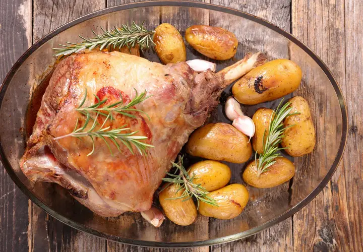 Gigot d'agneau rôti, doré et savoureux, accompagné de pommes de terre grenaille et d'ail, prêt pour la cuisson.
