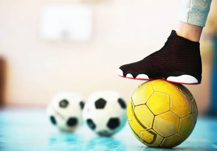 Stopa na żółtej piłce, w tle dwie białe. To pytanie: futsal co to?