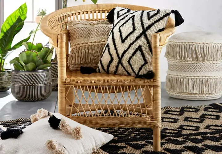 A rattan chair with decorative pillows and a fringed pouf, showcasing various types of fancy chairs and bohemian decor.