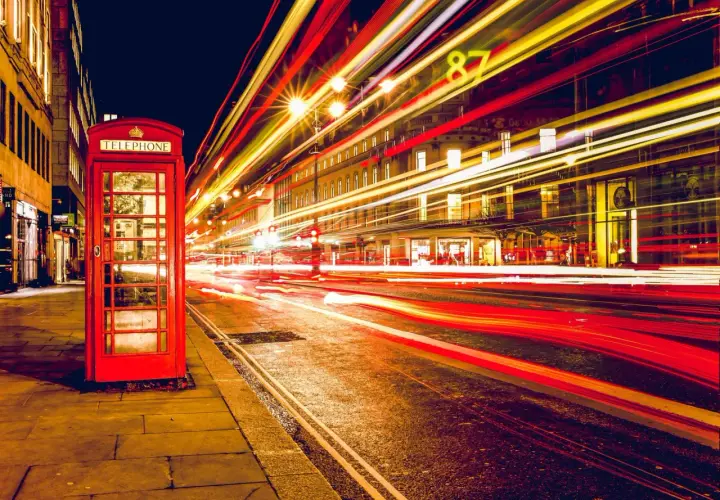 Klasyczna czerwona budka telefoniczna na tle nocnej ulicy z rozmazanymi światłami samochodów, efekt długi czas naswietlania zdjecia.