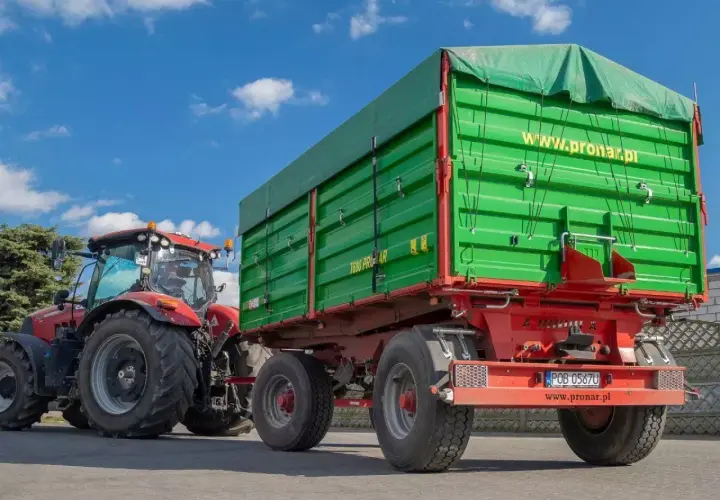 Czerwony traktor ciągnie zieloną przyczepę z plandeką. Duża masa przyczepy gotowa do pracy na polu.