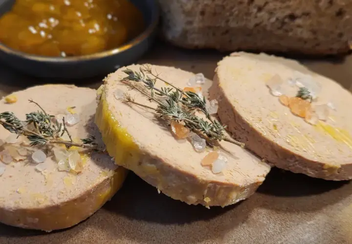 Trzy plastry foie gras, posypane solą i gałązkami tymianku, obok dżemu i chleba. Foie gras co to? Delikatesowy pasztet z gęsiej lub kaczej wątróbki.