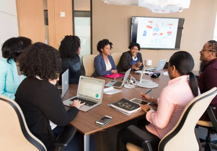 A diverse team collaborates in a meeting room, with one woman acting as an internal coach, guiding the discussion.
