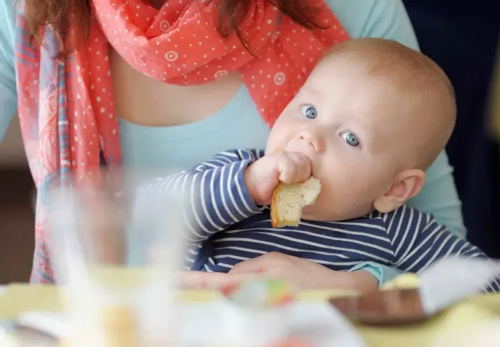 Bambino con occhi azzurri assaggia un pezzo di pane, un momento chiave per capire quando iniziare lo svezzamento.