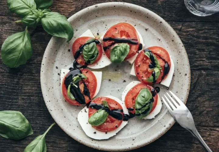 Tomate-Mozzarella-Salat mit frischem Basilikum und Balsamico-Glasur auf einem rustikalen Teller.