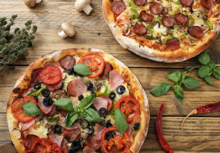 Dwie pizze z różnymi dodatkami: jedna z salami, papryką i pieczarkami, druga z szynką, pomidorami i oliwkami. Idealne na wspólne jedzenie, pokazujące jakie dodatki do pizzy wybrać.