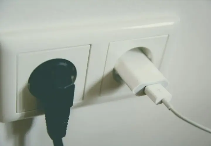 Gniazdko elektryczne z podłączoną czarną wtyczką i białą ładowarką. Urządzenia te, dzięki swojej konstrukcji, należą do drugiej klasy ochronności.