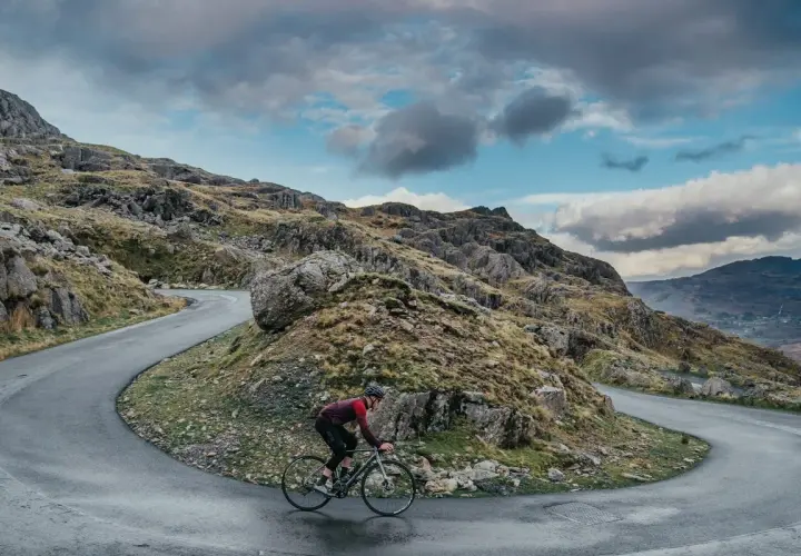 Ciclista en una carretera sinuosa en un paisaje montañoso, disfrutando de su aventura de España en bicicleta.