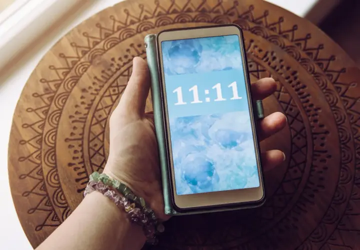 Dłoń z bransoletkami trzyma telefon z wyświetloną godziną 11:11. To znak, że 11.11 znaczenie ma dla wielu osób.