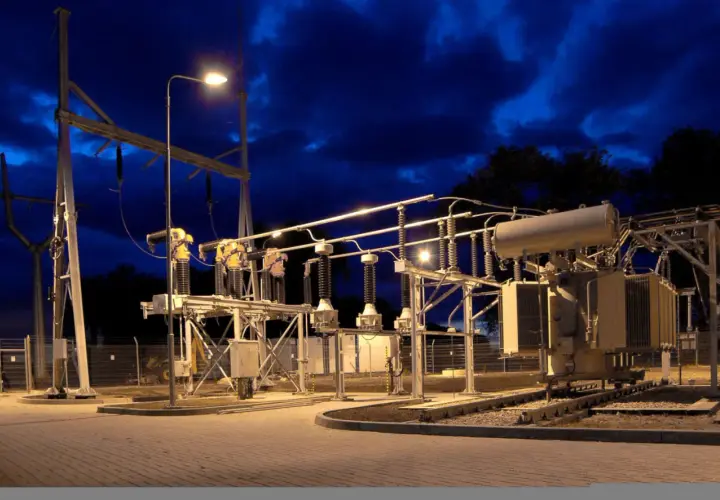 Nocna iluminacja podstacji trakcyjnej z transformatorem i izolatorami.