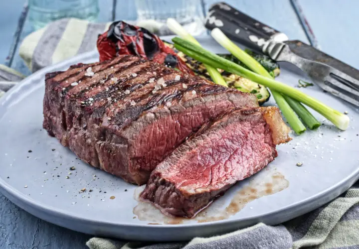 Un pavé de rumsteak grillé, coupé en tranches, servi avec des légumes rôtis et des oignons verts.