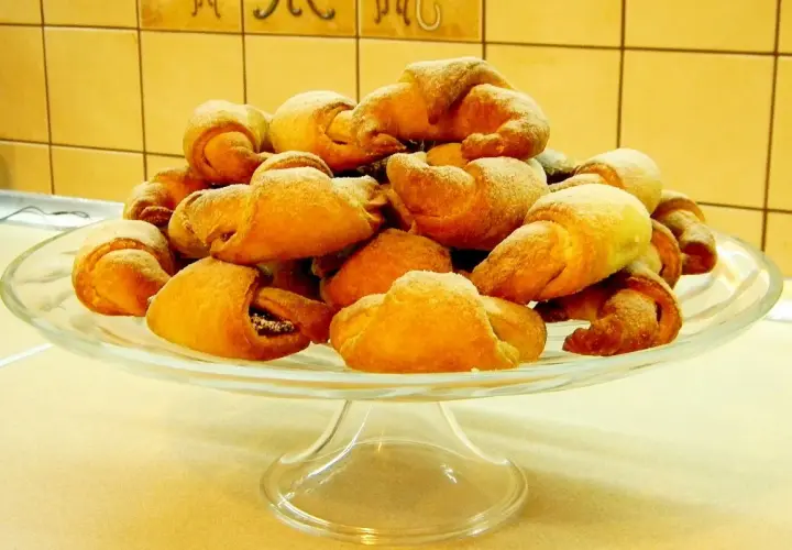 Stos rogalików drożdżowych, przygotowanych według przepisu babci, na szklanej paterze.