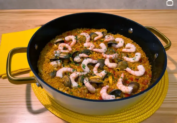 Arroz con gambones y almejas en paellera, listo para disfrutar.