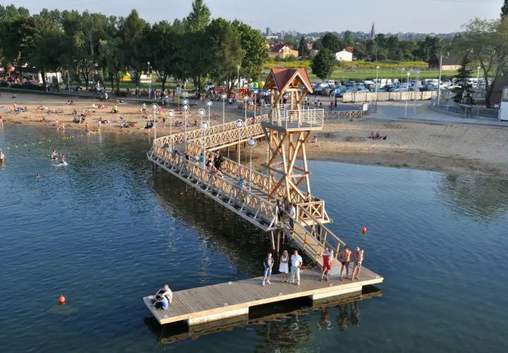 Ludzie odpoczywają na plaży i w wodzie przy drewnianym molo w Pogorii, Dąbrowa Górnicza.