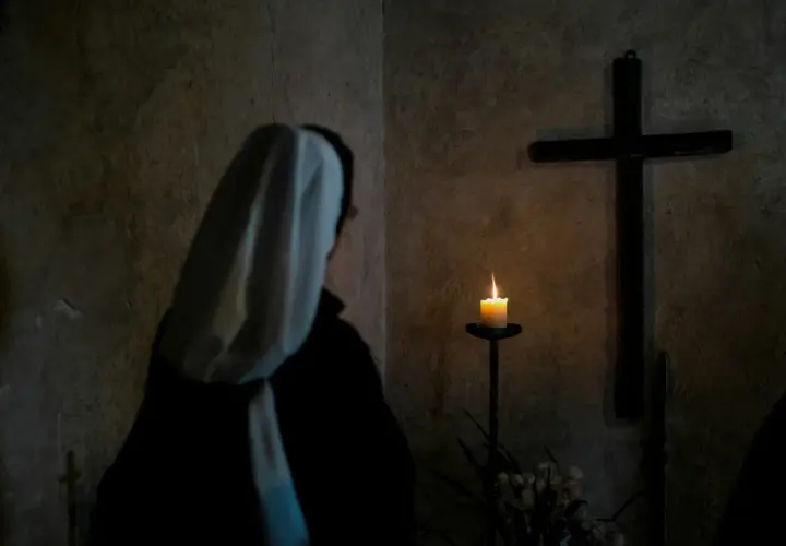 Zakonnica w ciemności przed krzyżem i płonącą świecą.