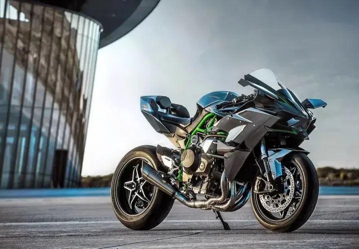 Czarny Kawasaki Ninja H2R, znany jako najszybszy motor na świecie, z zielonymi akcentami, stoi przed nowoczesnym budynkiem.