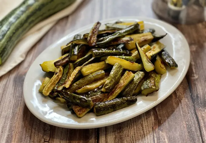 Zucchine al forno con pangrattato e parmigiano, dorate e croccanti, servite su un piatto bianco.
