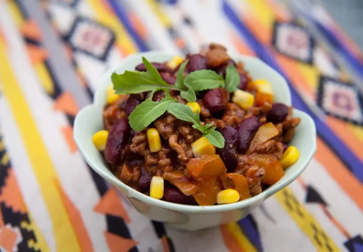 Miseczka pełna aromatycznego chili con carne przepis oryginalny, z fasolą, kukurydzą i mięsem mielonym, ozdobiona świeżymi ziołami.