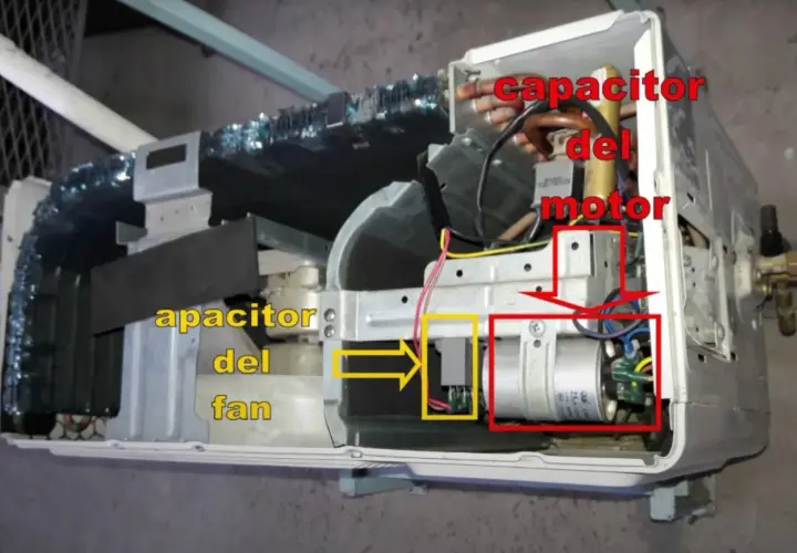 Componentes internos de un aire acondicionado, mostrando el capacitor del motor y el capacitor del fan.