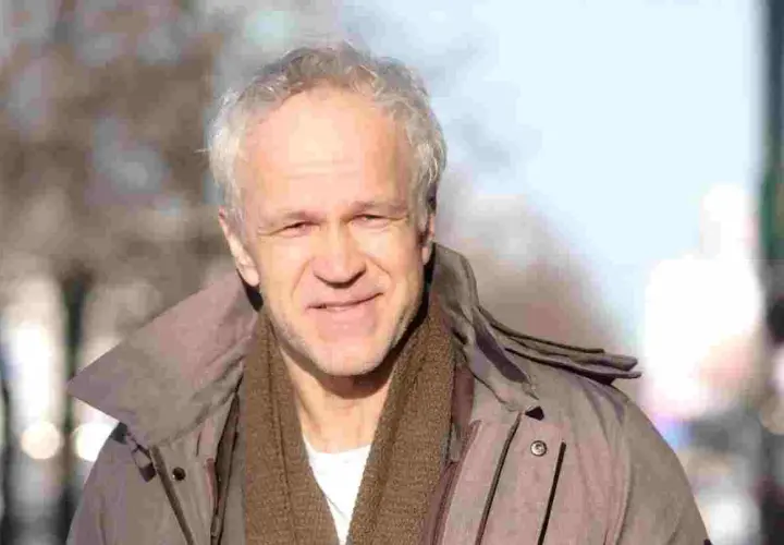 Uśmiechnięty Radosław Pazura w brązowym szaliku i kurtce, przypomina o swoich niezapomnianych rolach w polskich filmach.
