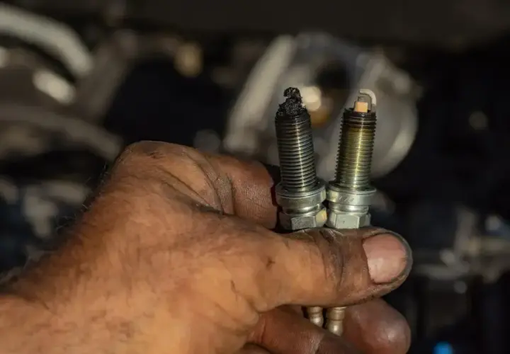 Brudne ręce mechanika trzymają dwie świece zapłonowe. Jedna jest mocno okopcona, co może sugerować problemy z silnikiem. Czy diesel ma świece zapłonowe? Nie, diesel nie ma świec zapłonowych.
