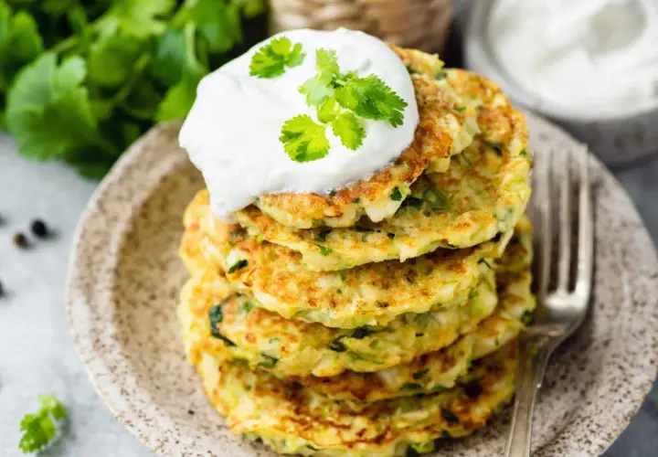 Pile de beignets de courgettes à l'italienne, garnis d'une cuillère de crème et de coriandre fraîche. Un délice croustillant et savoureux.