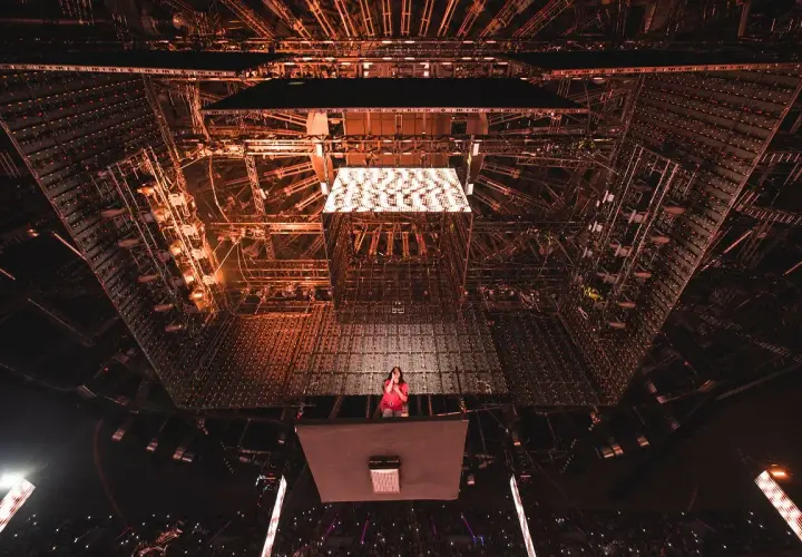 Billie Eilish na scenie, otoczona skomplikowaną konstrukcją oświetleniową. Tekst piosenki "NDA" rozbrzmiewa w tłumie.