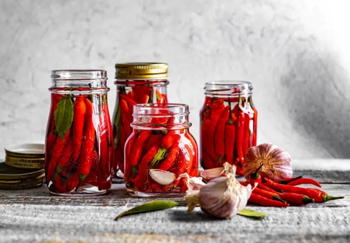 Słoiki z papryczkami chili w zalewie, obok czosnek i świeże papryczki. Idealne do pikantnych potraw.