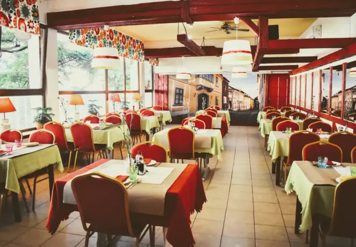 Wnętrze restauracji z czerwonymi krzesłami i stolikami nakrytymi na przyjęcie. Mural z ulicą przypomina czardasz Gdańsk.
