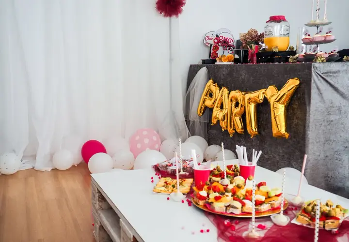 Urocze pomysły na wieczór panieński w domu: złote balony z napisem "PARTY", przekąski i różowe akcenty.