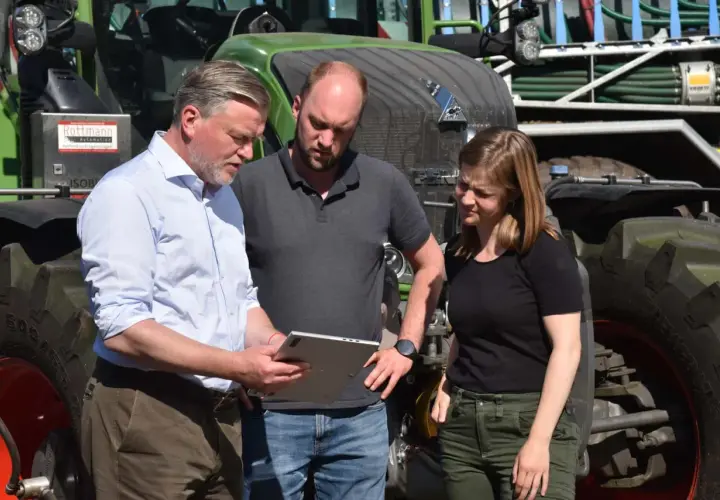 Drei Personen besprechen auf einem Tablet die **Pauschalierung in der Landwirtschaft** vor einem grünen Traktor.