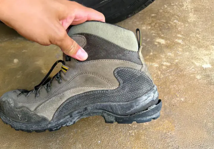 A hand holds a worn hiking boot, showing why shoe soles crack: exposure to elements and heavy use can cause the rubber to degrade and split.