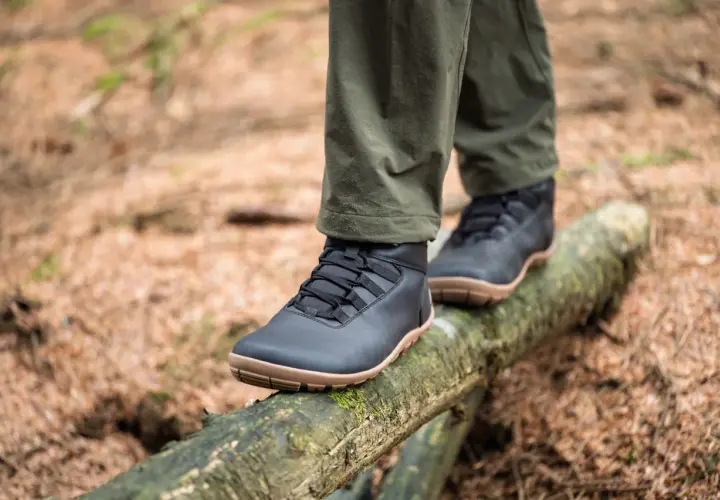 Black, low-profile shoes with tan soles, perfect as shoes to wear in winter besides boots, balance on a mossy log in a forest.