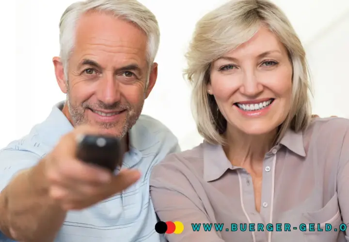 Glückliches Rentnerpaar mit Fernbedienung. Informieren Sie sich über die GEZ-Befreiung für Rentner und die Einkommensgrenze auf www.buerger-geld.org.