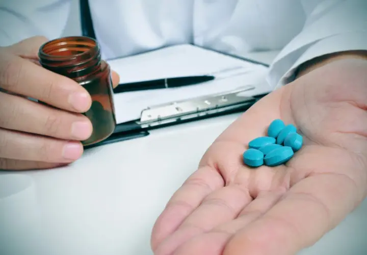 Lekarz podaje kilka niebieskich tabletek, prawdopodobnie ketoprofen, na dłoń.