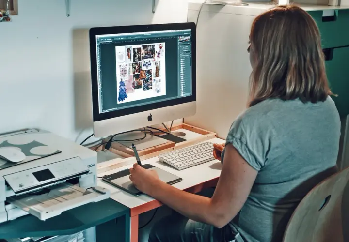 Une graphiste textile travaille sur son ordinateur, créant des moodboards et des designs. Une imprimante est visible à côté.