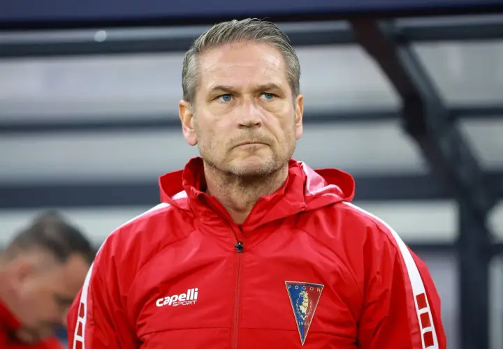 Twarz trenera Pogoni Szczecin, zamyślony, w czerwonej kurtce sportowej z herbem klubu.