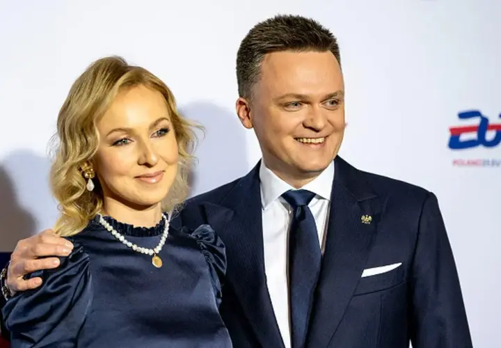 Szymon Hołownia z żoną, uśmiechnięci, pozują do zdjęcia. Ona w granatowej sukience i perłach, on w garniturze.