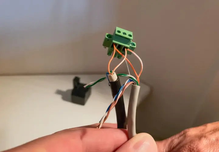 Connexion de fils électriques à un domino vert. Un câble noir et un câble gris sont dénudés, leurs fils colorés prêts pour le domino.