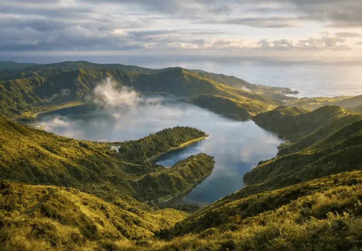 Widok z góry na jezioro w kraterze w otoczeniu zielonych wzgórz i oceanu.
