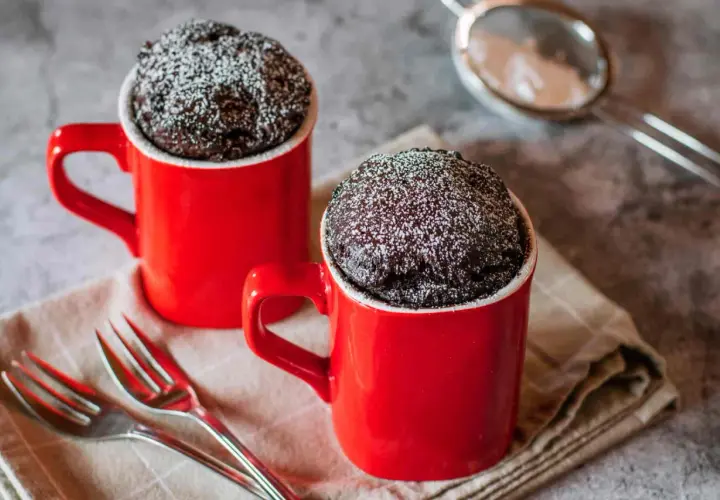 Due tortine in tazza al microonde, ricoperte di zucchero a velo, pronte per essere gustate con due forchettine.