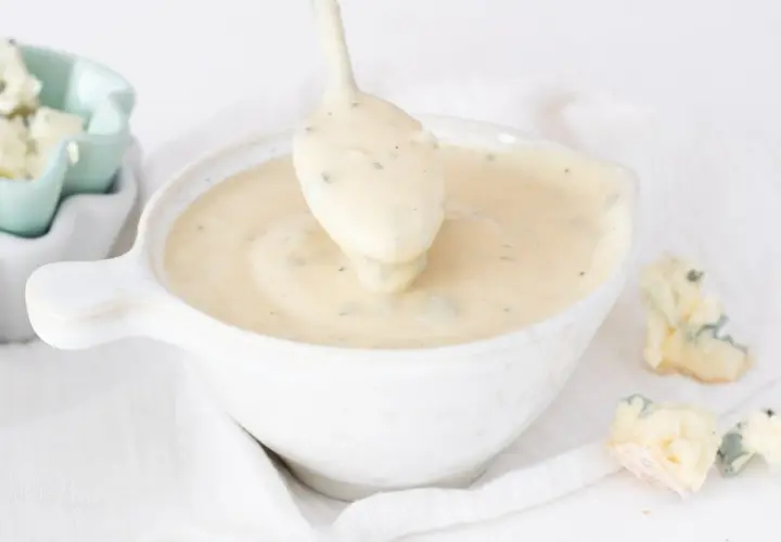 Cremosa salsa gorgonzola servida en un cuenco blanco, con trozos de queso gorgonzola esparcidos alrededor.