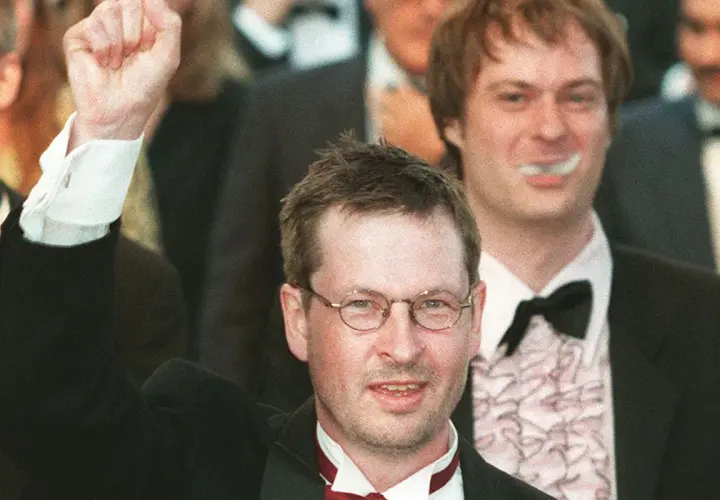 Lars von Trier, regista, alza il pugno in segno di vittoria, circondato da festeggiamenti.