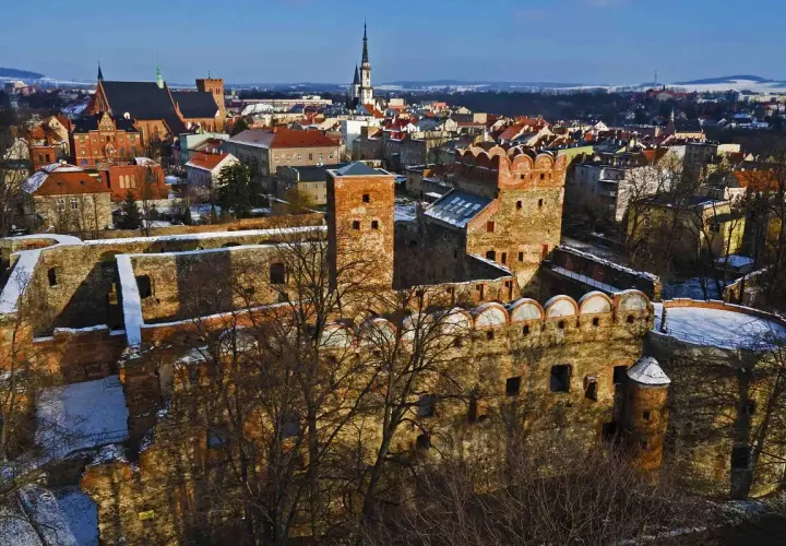 Ruiny zamku w Ząbkowicach Śląskich, z charakterystycznymi ceglanymi murami i wieżami, na tle zimowego krajobrazu miasta.